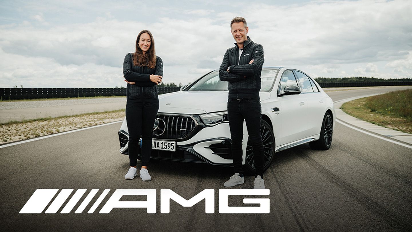 Zwei Personen stehen mit verschränkten Armen vor einem weißen Mercedes-AMG E 53 Sedan Hybrid auf einer Teststrecke