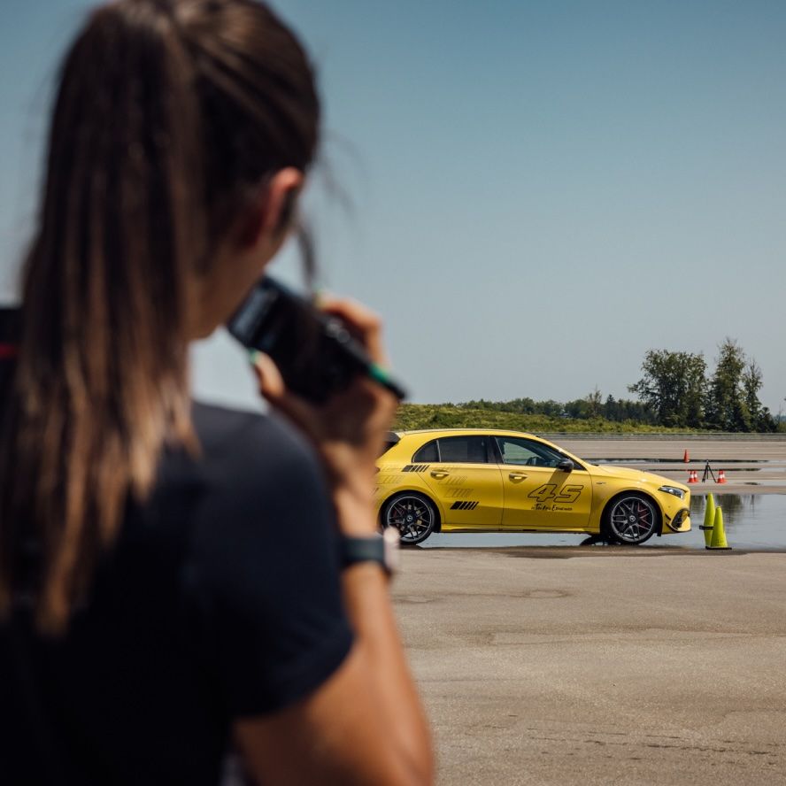 Eine Frau spricht in ein Walkie-Talkie, im Hintergrund ist ein gelber AMG zu sehen.
