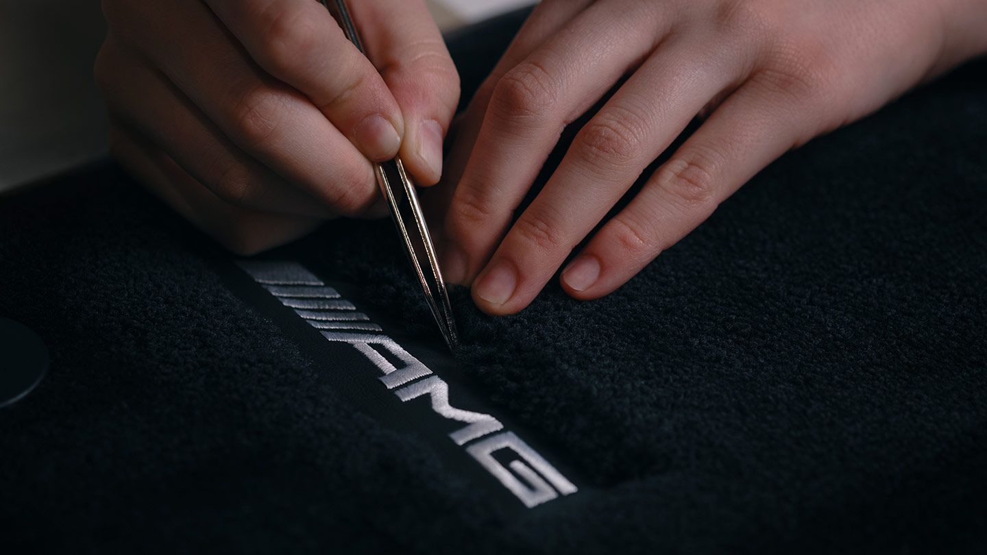 Zwei Hände im Fokus beim Nähen des AMG Schriftzuges.